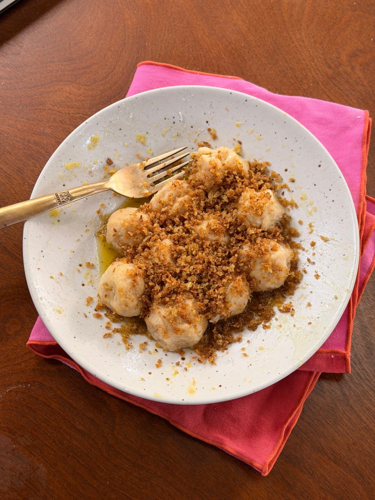 A plate of dumplings topped with breadcrumbs and drizzled with oil, resting on a vibrant pink napkin.